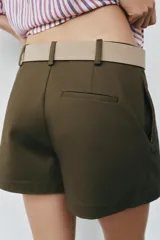 Falda pantalón de tiro medio en color verde militar, con diseño de pliegue delantero y cierre lateral con cremallera oculta. Incluye un cinturón ancho en tono tostado con hebilla metálica ovalada.