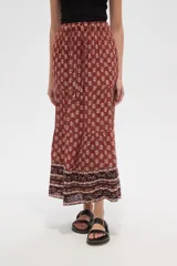 Falda larga de viscosa con estampado en tonos terracota y beige. Presenta un diseño escalonado con un patrón floral repetitivo en la parte principal y un borde inferior con un patrón geométrico en tonos más oscuros. Tiene cintura elástica con cordón ajustable.
