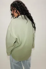 Camisa oversize color verde menta, con cuello camisero, cierre frontal de botones, bolsillo de parche en el pecho y mangas anchas por debajo del codo.