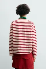 Camiseta de manga larga con diseño de rayas horizontales en color rojo y crema. Presenta cuello redondo con ribete a contraste y un pequeño parche bordado en el pecho.