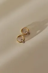 Par de aros tipo argolla dorados de acero quirúrgico, con una piedra natural de color gris translúcido colgando de cada uno.