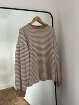 Sweater de punto con diseño de rayas horizontales en color beige y blanco, cuello redondo y puños acanalados en color beige sólido.