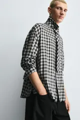 Camisa de corte relajado confeccionada en tejido fluido con estampado de cuadros. Presenta cuello solapa, cierre frontal de botones, manga larga con puños abotonados y una corbata integrada del mismo tejido.