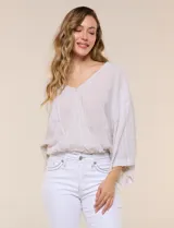 Blusa de algodón y rayón color beige, de la marca Dash. Presenta diseño texturado con sutiles rayas verticales, escote en V cruzado, mangas tres cuartos amplias y ruedo elastizado.