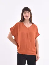 Blusa de corte holgado color naranja, con escote en V y mangas cortas tipo murciélago. Presenta una costura vertical central en el frente y una textura sutilmente arrugada.