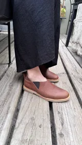 Zapatos tipo chelsea de cuero color marrón, con paneles elásticos laterales y suela plana de goma.