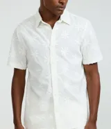 Camisa de manga corta color blanco con diseño bordado de flores, cuello inglés y cierre frontal de botones.