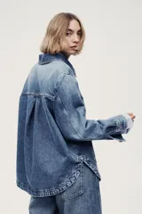 Campera camisera en denim rígido con cuello, cierre frontal de botones, puños abotonados, bolsillos de parche delanteros y dobladillo redondeado.
