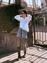 Falda midi de tapicería con rayas verticales en tonos grises y apliques de cuero bordados a mano. Presenta flecos largos en el ruedo.