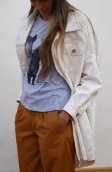 Chaqueta larga de acrocel color blanco crudo, con cuello camisero, hombros caídos, bolsillos con solapa en el pecho y terminación desflecada.