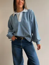 Buzo tipo chomba de corte oversize con diseño a rayas horizontales celestes y blancas. Presenta cuello camisero blanco y un bordado en la espalda con la inscripción República Oriental del Uruguay.