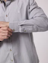 Camisa de manga larga a rayas verticales azules y blancas, con cuello abotonado y logo de la marca bordado en el pecho.