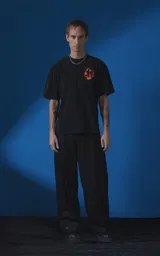 Remera de manga corta con cuello redondo y calce oversize, color negro con efecto nevado. Presenta una estampa frontal en color naranja con diseño gráfico de un rostro rodeado de llamas y texto tipográfico.