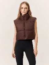 Chaleco puffer de corte cropped y diseño acolchado, con cuello alto y cierre frontal completo. Presenta un acabado liso en color marrón oscuro.