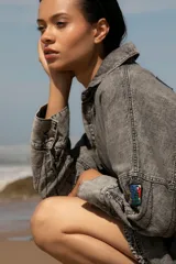 Vestido camisero corto de denim azul, con cuello camisero, cierre frontal con botones y mangas largas con puños abotonados.