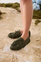 Mocasines de gamuza color verde militar, con diseño de flecos alrededor del calzado, capellada con cordón decorativo y detalles de avíos dorados.
