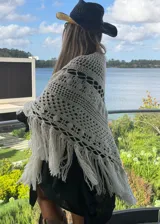Ruana tejida artesanalmente en lana merino, con diseño de calados geométricos y terminación de flecos largos en el ruedo.