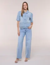 Camperita de denim color celeste con efecto lavado suave, cuello camisero clásico y cierre frontal de botones metálicos. Tiene mangas cortas con fruncido en los hombros, bolsillos delanteros bajos y costuras estructuradas.
