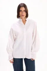 Camisa blanca de corte oversize con textura de rayas verticales sutiles. Presenta cuello mao, cierre frontal con botones y mangas largas abullonadas con puños anchos.