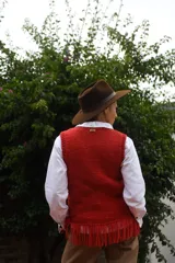 Chaleco de punto tejido a mano con lana merino, color blanco, con cuello redondo, detalles de flecos en el ruedo y aplique de etiqueta de cuero con la marca.