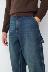 Jean de corte relaxed estilo carpintero, en tono azul oscuro con efecto lavado. Presenta diseño de cinco bolsillos, incluyendo bolsillos laterales utilitarios, cierre de botón y cremallera, y costuras reforzadas.