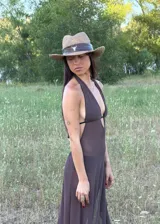 Vestido largo de color chocolate, con escote halter profundo y diseño de falda con volados laterales. Presenta una silueta fluida y transparente.