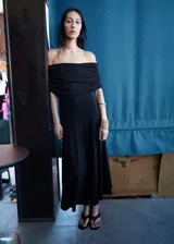 Vestido midi negro con escote bote de hombros caídos y diseño evasé, sin mangas.
