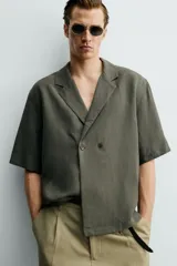Camisa tipo kimono de corte relaxed fit, color celeste, confeccionada en tejido fluido de viscosa y lino. Presenta cuello con solapas de muesca, manga corta y cierre frontal cruzado con doble botonadura.