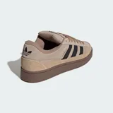 Championes Adidas Campus ST de estilo urbano inspirado en los años 90. Presentan un exterior de gamuza y lona en tonos marrones con las icónicas tres tiras laterales en color negro. Cuentan con suela de caucho resistente y cierre mediante cordones.