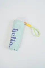 Paraguas plegable color verde agua con la palabra 'hello.' estampada en color violeta. Incluye una correa de muñeca en color amarillo neón.