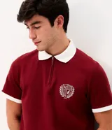 Remera polo azul marino con cuello y puños en contraste de color blanco, manga corta y cierre frontal parcial. Presenta un escudo bordado en el pecho.