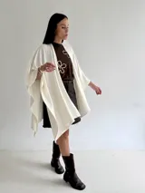 Ruana de tejido de punto trenzado en color crudo, con diseño abierto, corte holgado y mangas amplias tipo kimono.