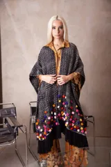 Poncho tipo ruana tejido en telar artesanal, color negro con textura de puntos blancos y decorado con pompones multicolores y flecos largos en los bordes.