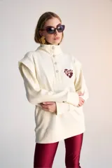 Buzo color crudo de algodón pima, con cuello alto con botones y detalle bordado de corazón en el pecho.