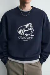 Sudadera azul marino de algodón, corte relajado (relaxed fit) con cuello redondo y manga larga. Presenta un estampado frontal en blanco con un caballo en movimiento rodeado por una cuerda y el texto "Bold Spirit".