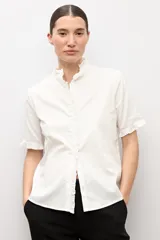 Camisa blanca de manga corta con cuello mao y detalles de volados a lo largo de la botonera frontal y en los puños.