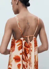 Vestido largo de corte recto y tejido fluido, con estampado de palmeras en tonos naranjas sobre fondo crema. Presenta cuello halter con detalle fruncido, tirantes finos ajustables y cierre de lazo en la espalda.
