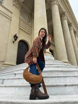 Cartera tipo hobo de cuero gamuzado color camel, con correa ajustable y etiqueta de cuero con logo grabado en el frente.