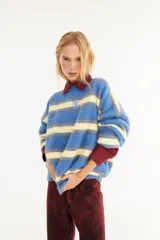 Sweater de textura peluda con diseño de rayas horizontales en tonos bordó, amarillo y azul. Presenta un corte holgado, cuello redondo y un pequeño logo bordado en el centro del pecho.