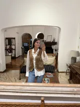 Chaleco marrón de corte corto con bordados florales en color crema en el frente y cierre frontal con botones. Presenta un diseño estructurado con cuello camisero.