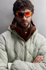 Campera puffer verde oliva acolchada con diseño de rombos, capucha y cierre frontal con cremallera. Incluye bolsillos laterales con cierre. Relleno de plumón y plumas.