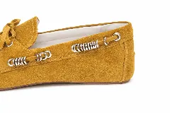 Mocasines de gamuza color mostaza, con detalles de anillos metálicos plateados en los laterales y cordones decorativos en el empeine.