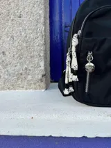 Mochila negra de nylon con cierre plateado y etiqueta con el logo de la marca en color beige.