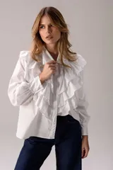 Camisa blanca de corte clásico con volados frontales y en los hombros, manga larga con puños abotonados y cierre frontal con botones.