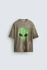 Camiseta de corte relajado con cuello redondo y manga corta. Presenta un efecto de lavado desgastado en tonos marrones y un estampado frontal de una cabeza de alienígena en color verde vibrante.