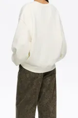 Buzo cropped de corte recto, color blanco hueso, con cuello redondo y mangas largas amplias. Presenta un estampado frontal de estilo ilustrativo con un paisaje nocturno, árboles, cisnes volando y una luna creciente, con tonos verde agua y naranja para las estrellas.