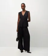 Pantalón de sastrería color negro, con cintura estructurada, pliegues delanteros, corte recto y cierre asimétrico.