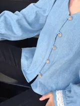 Camisa celeste de jean con cuello en V, mangas largas abullonadas con puños de encaje y cierre frontal con botones.