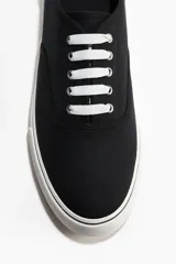 Calzado deportivo de lona de algodón en color negro con cordones blancos y suela de goma blanca con detalles en negro.