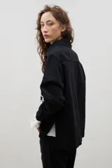 Camisa de denim negro con estampa floral blanca, cuello camisero, cierre frontal con botones y mangas largas.